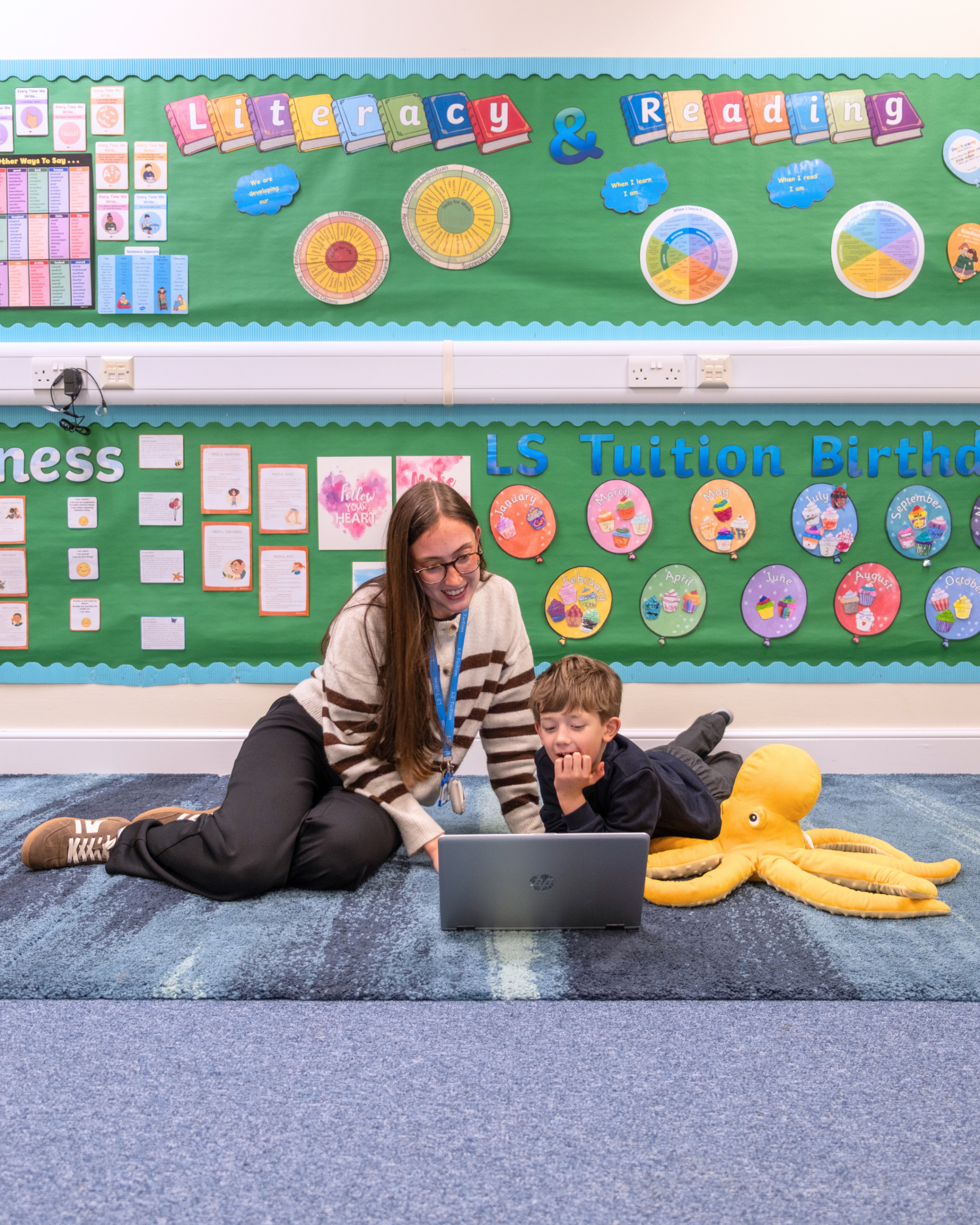 A tutor and student sit on the carpet learning sounds on a laptop